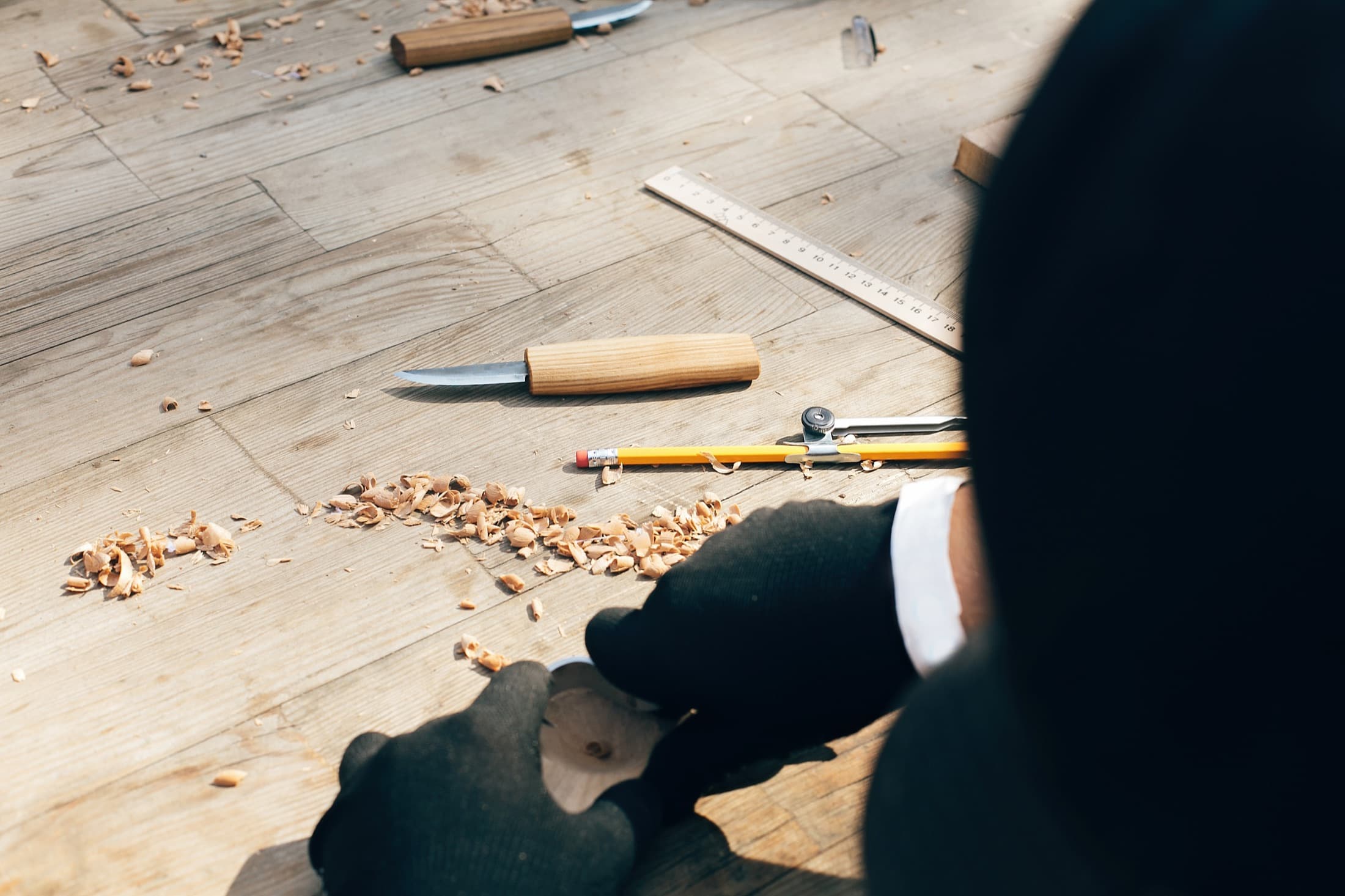 Hands working at a wooden surface with carving tools, ruler, pencil, and shavings — the craft discipline behind 22 years of inspection reports.